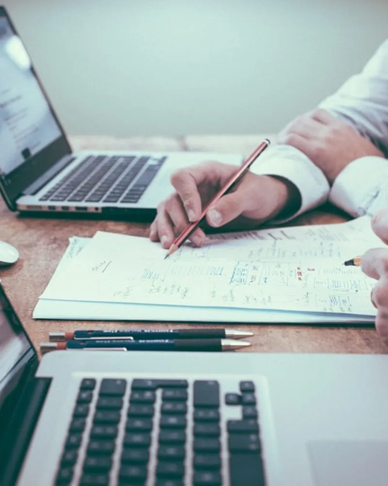 Dos personas trabajan una estrategia sobre un cuaderno, entre dos portátiles