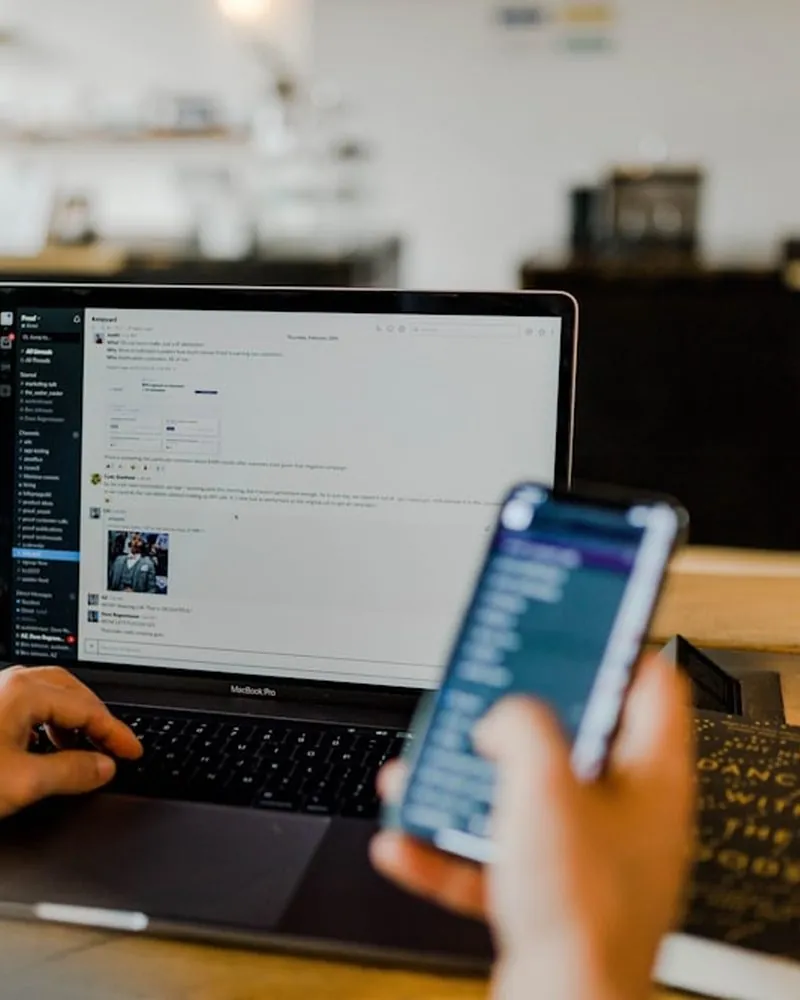 Una persona revisa un feed de redes sociales en el móvil mientras trabaja con el portátil