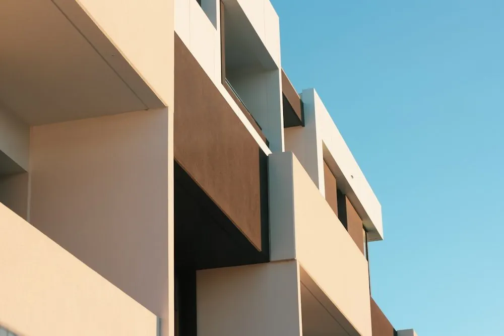 Fachada de un edificio residencial moderno en tonos hueso, contra un cielo azul despejado